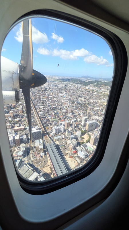 窓越しに見える飛行機のプロペラと福岡の街